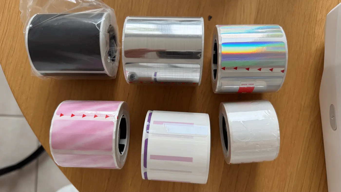 Rouleaux d’étiquettes NIIMBOT de différentes formes et finitions : noires, argentées, holographiques, roses et blanches