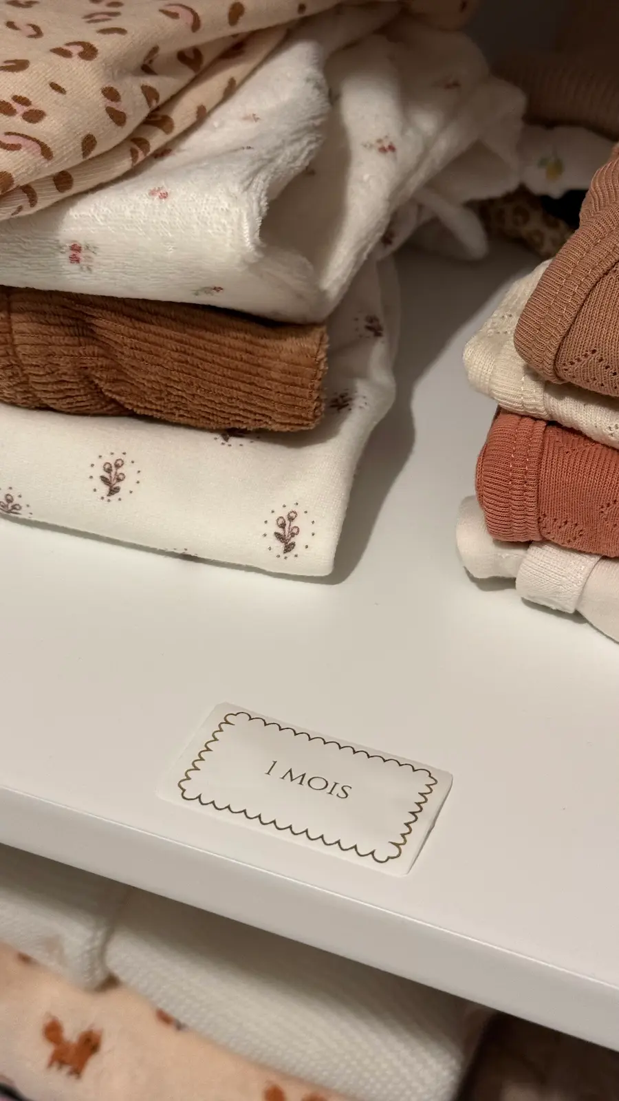 Étiquette 1 mois avec un cadre décoratif sur une étagère de vêtements de bébé