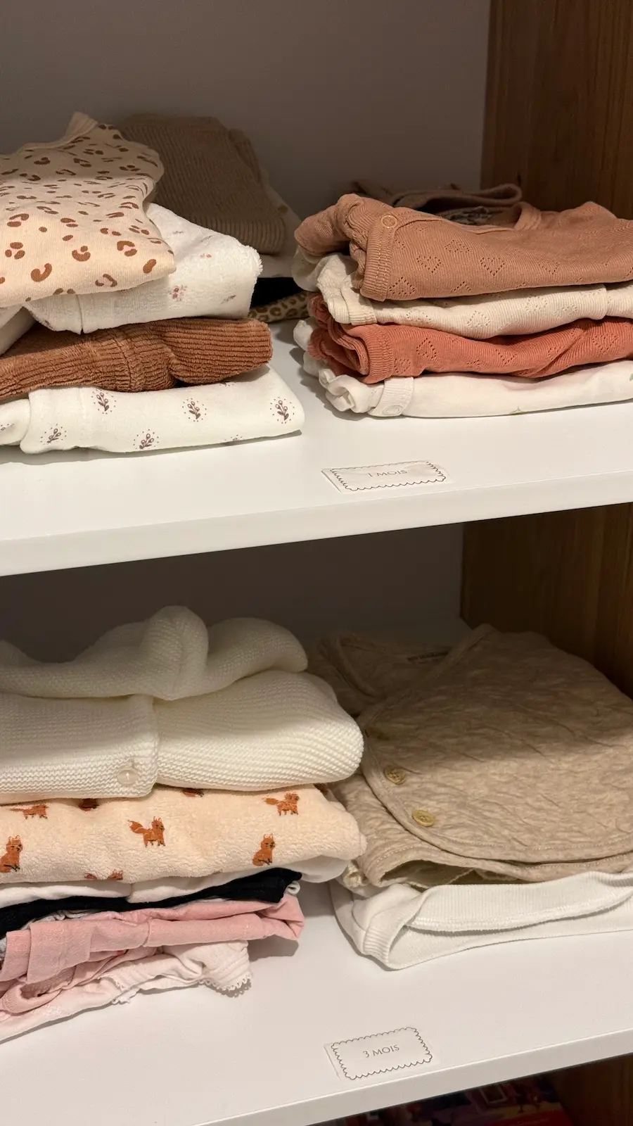 Vêtements de bébé rangés sur des étagères étiquetées 1 mois et 3 mois avec l'imprimante Niimbot M2